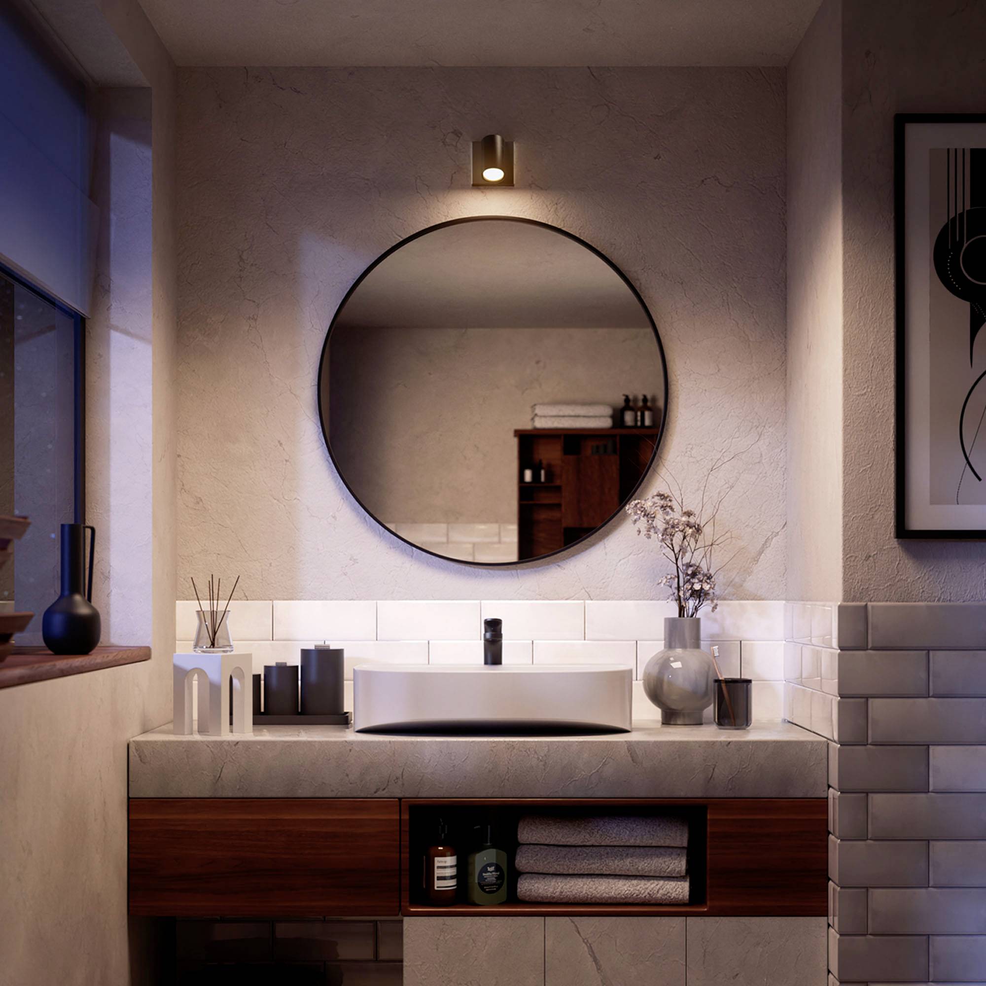 Modernes Badezimmer mit rundem Spiegel, Waschbecken auf Holzunterschrank, dekorativen Objekten und stimmungsvollem Licht.