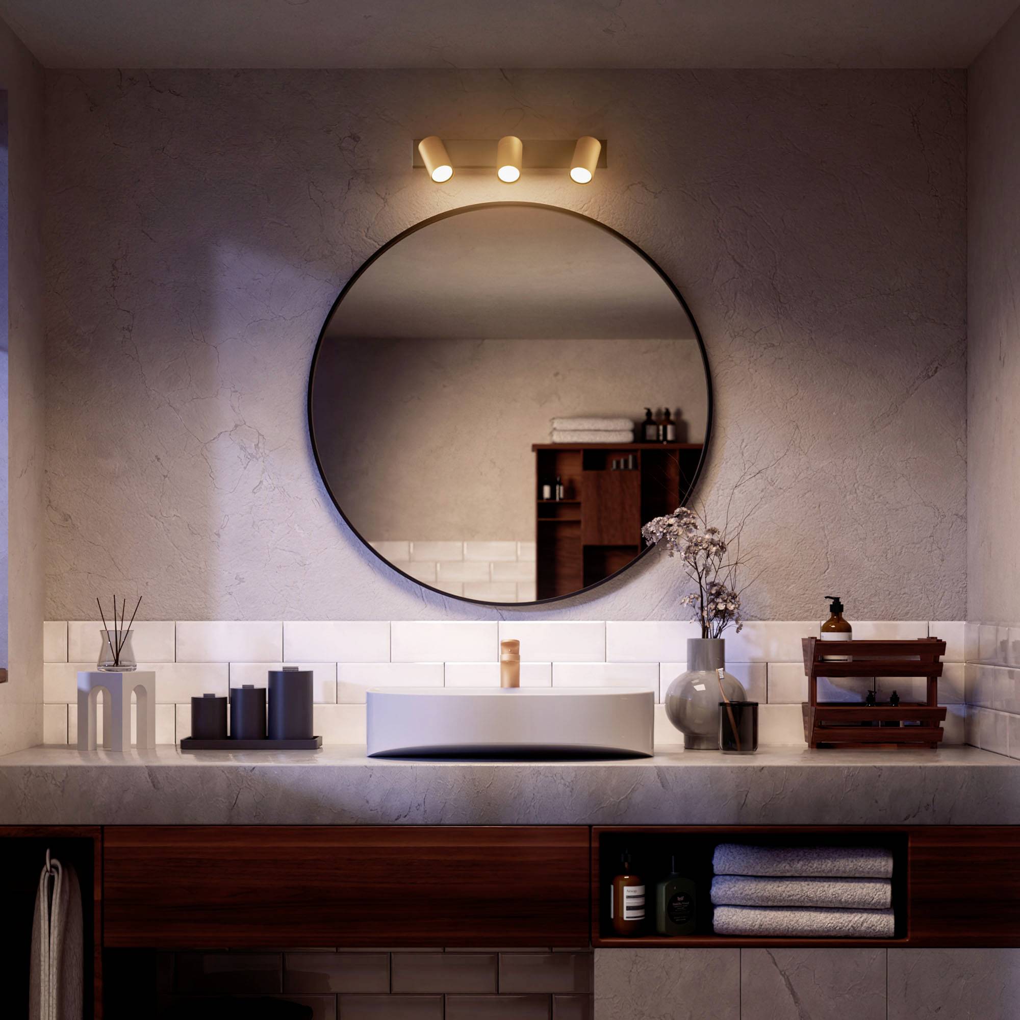 Modernes Badezimmer mit rundem Spiegel über einem Waschbecken, flankiert von weißen Fliesen. Beleuchtung oben, Glasvase mit Zweigen rechts.