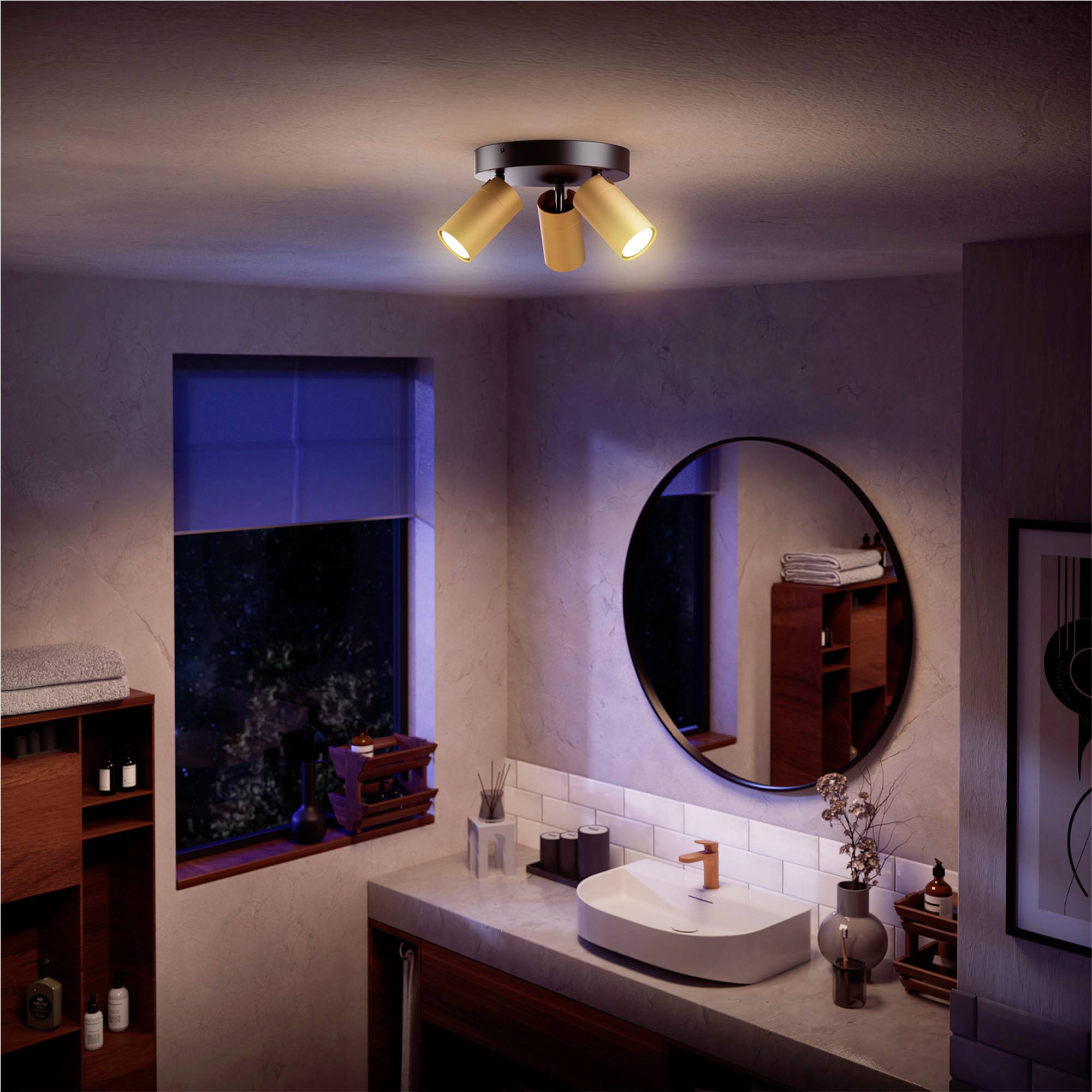 Badezimmer mit Spiegel, Waschbecken und modernem, dreiflammigem Deckenstrahler, der warmes Licht abstrahlt. Gemütliche Atmosphäre.
