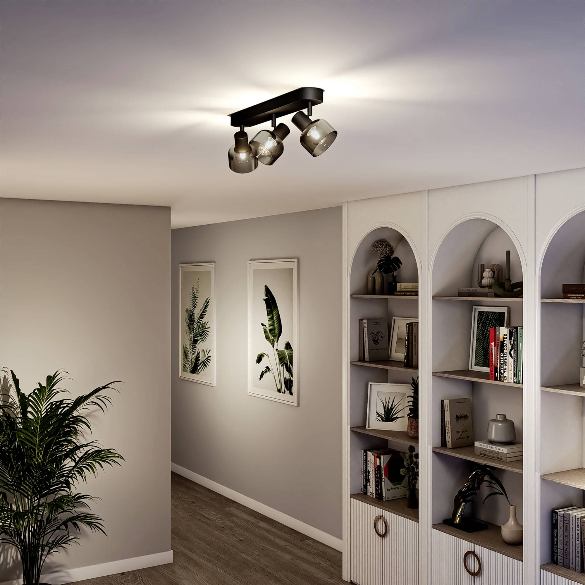 Eine elegante Wohnzimmerbeleuchtung mit drei Strahlern an der Decke. Daneben stehen ein Bücherregal und Pflanzen für ein gemütliches Ambiente.