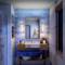 Ein modernes Badezimmer mit blau gefliester Wand, Waschbecken mit Holzunterschrank und beleuchtetem Spiegel. Links eine Dusche.