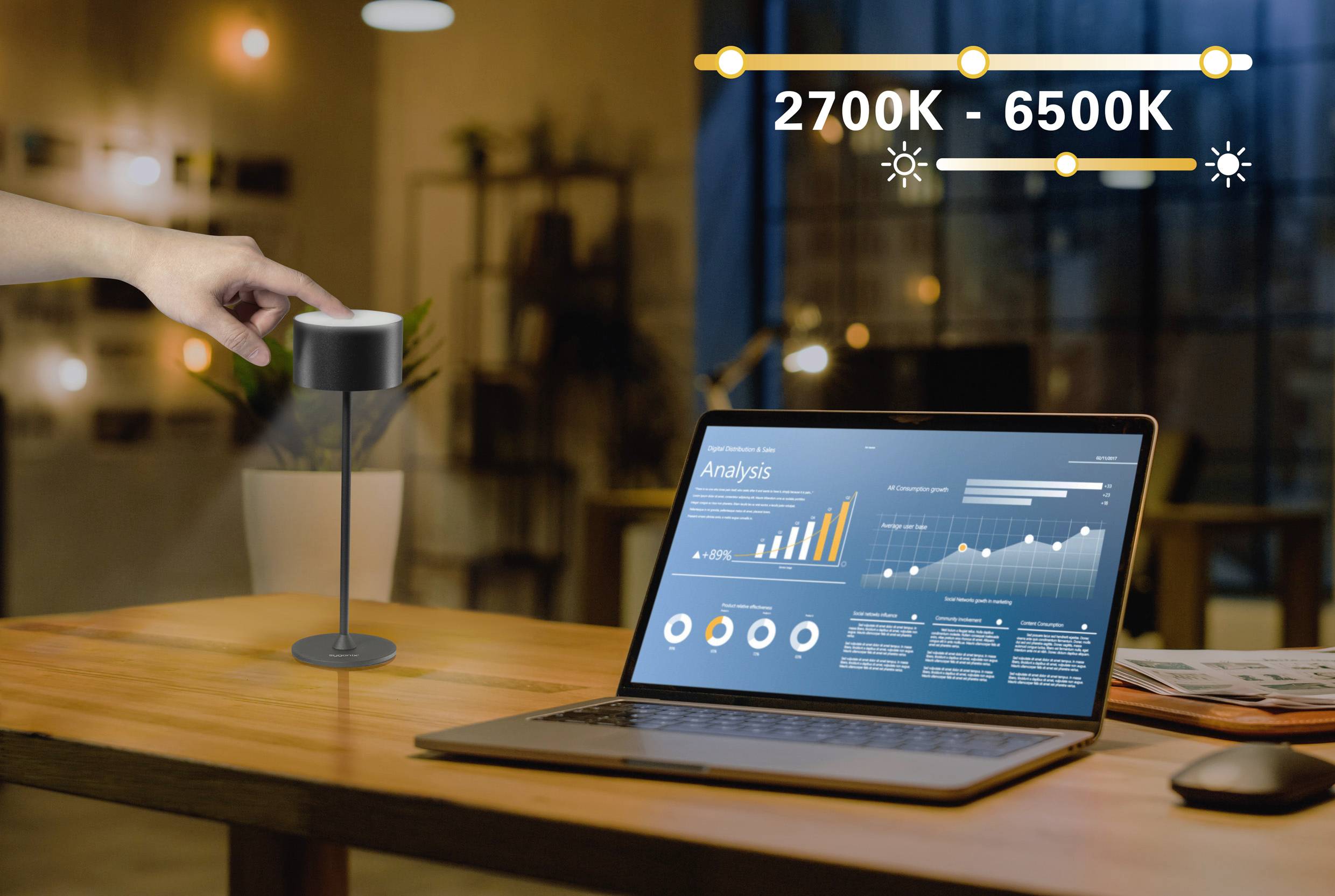 Eine Hand berührt eine Lampe auf einem Tisch neben einem Laptop mit Datenanalyse-Diagrammen auf dem Bildschirm; Aufschrift '2700K - 6500K'.