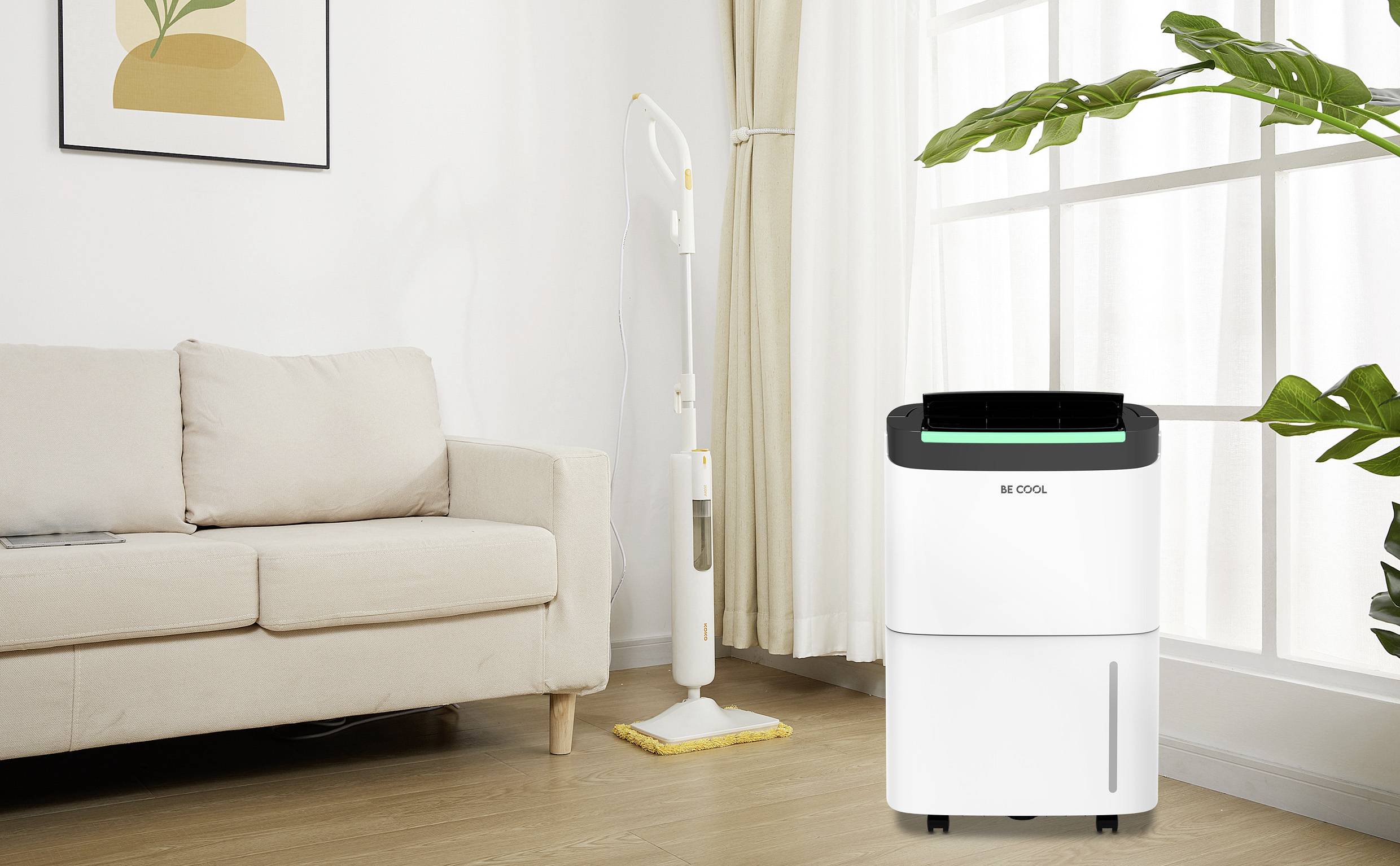 Luftentfeuchter im Wohnzimmer neben einem Sofa und einer Pflanze. Helle Vorhänge und ein Bild an der Wand sorgen für eine gemütliche Atmosphäre.
