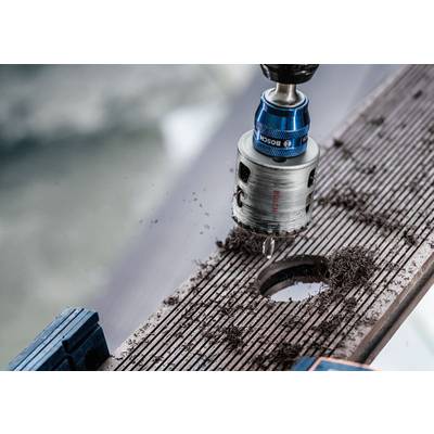 Bohrmaschine mit Bohreraufsatz fräst ein Loch in eine Holzplatte. Holzspäne sind um das gebohrte Loch verteilt.