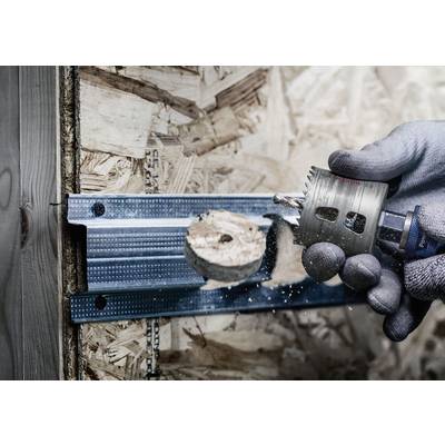 Eine Person bohrt mit einem Lochsägeaufsatz ein rundes Loch in eine Wand aus Sperrholz und Metallverstrebung. Fragment wird entfernt.