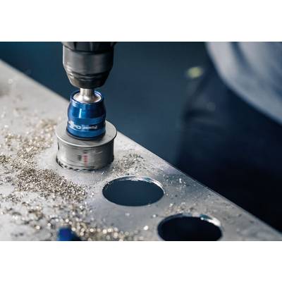 Bohrmaschine mit Lochsäge schneidet durch Metallplatte, erzeugt runde Löcher, Späne um das Werkzeug herum.
