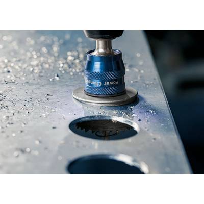 Nahaufnahme eines blauen Bohrers, der ein kreisförmiges Loch in eine Metallplatte bohrt, umgeben von Metallspänen.