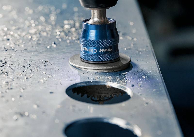 Eine blaue Bohrmaschine durchbohrt eine Metallplatte, wobei Metallspäne um das Bohrloch verstreut sind.