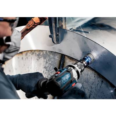 Eine Person bohrt mit einem Bohrgerät ein großes Metallrohr. Schutzkleidung und Handschuhe werden getragen.