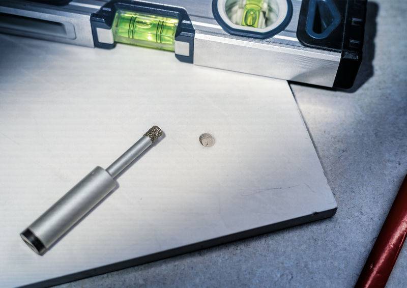 Bohraufsatz und Wasserwaage auf einer Steinplatte, vorbereitet für präzises Bohren.