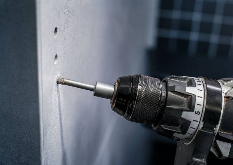 Ein Bohrer bohrt präzise Löcher in eine graue Betonwand. Der Bohrer hat ein schwarzes Metallgehäuse mit Skala.