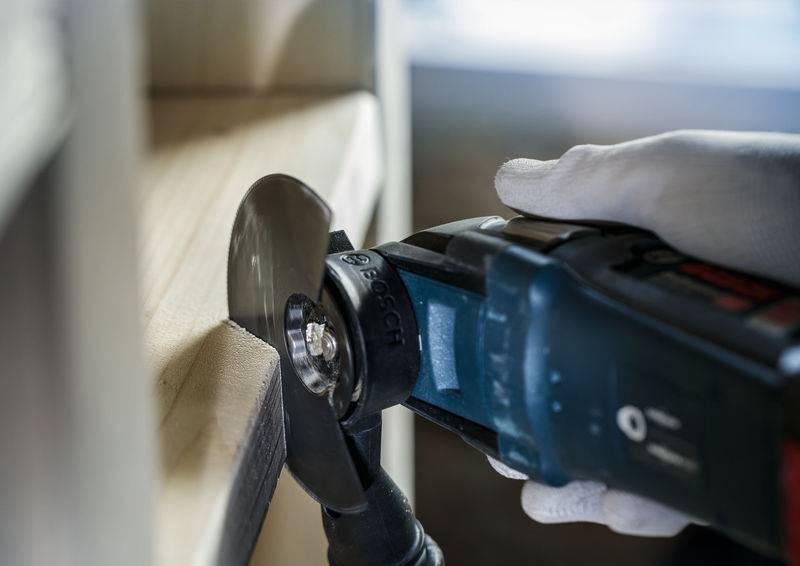 Eine Person mit Handschuhen nutzt ein Elektrowerkzeug, um Holz präzise zu schneiden. Fokus auf der Klinge und der Hand.