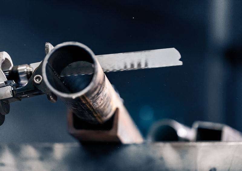 Metallrohr wird von einer Metallsäge geschnitten. Der Fokus liegt auf dem präzisen Sägeblatt, das durch das Rohr schneidet.