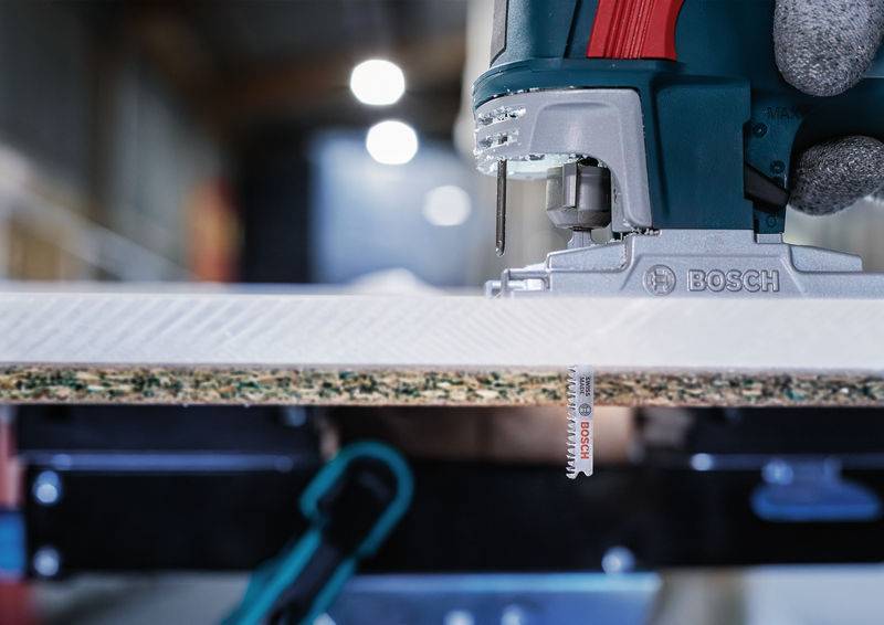 Eine Stichsäge schneidet eine Holzplatte in einer Werkstatt. Die Nahaufnahme zeigt die Säge in Aktion, gehalten von einer behandschuhten Hand.