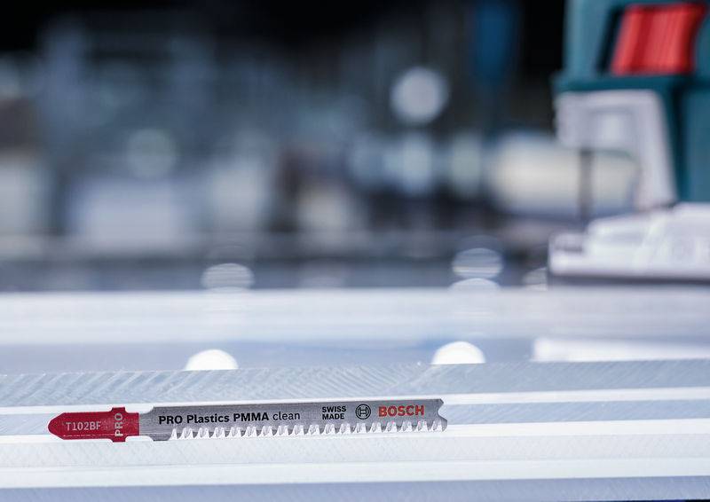 Ein rotes Bosch-Sägeblatt liegt auf einem glänzenden Tisch. Im Hintergrund ist unscharf eine Werkzeugmaschine zu sehen.