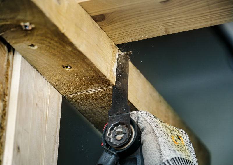 Eine Person schneidet mit einem oszillierenden Werkzeug ein Holzstück. Sie trägt einen Arbeitshandschuh.
