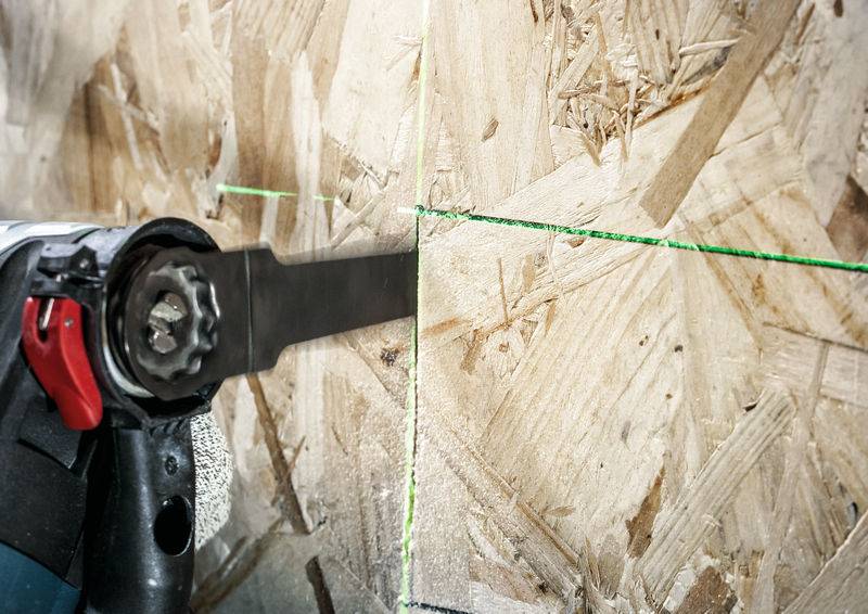 Nahaufnahme einer Kreissäge, die durch eine Holzplatte schneidet. Eine grüne Laserlinie zeigt die Schnittführung an.