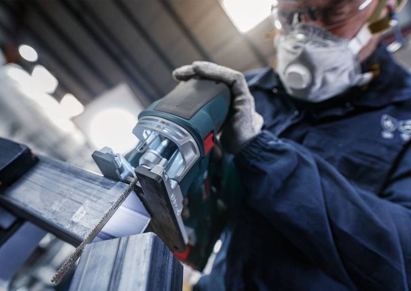 Ein Arbeiter trägt Schutzbrille und Maske, während er mit einer Elektrosäge Metall bearbeitet. Sicherheit bei der industriellen Metallverarbeitung.