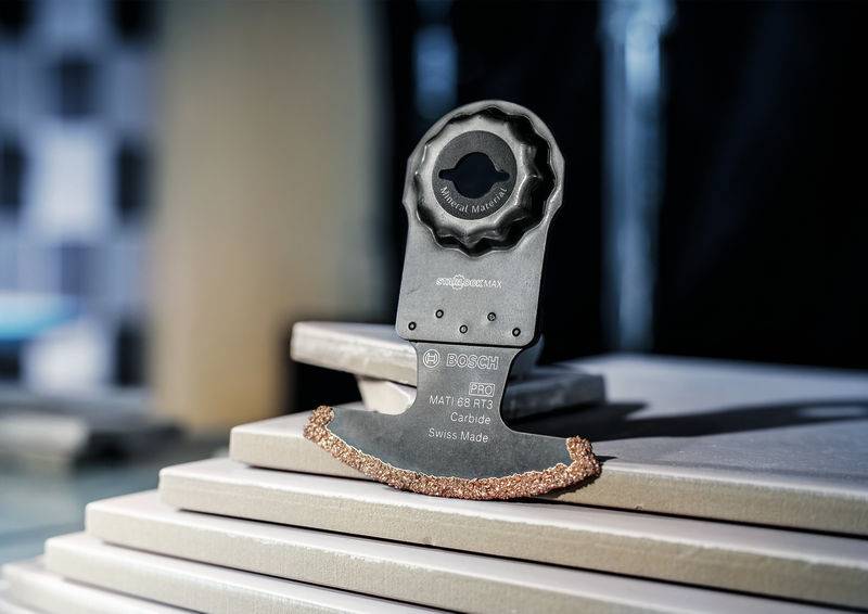 Ein oszillierendes Sägeblatt liegt auf gestapelten Kacheln, bereit für präzises Schneiden. Umgebung unscharf im Hintergrund.