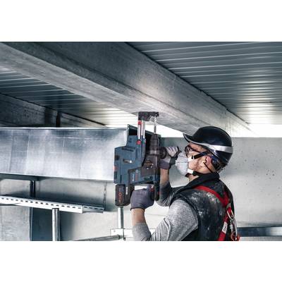 Ein Arbeiter mit Schutzhelm und Maske befestigt ein Metallgerät an einer Decke in einer industriellen Umgebung.