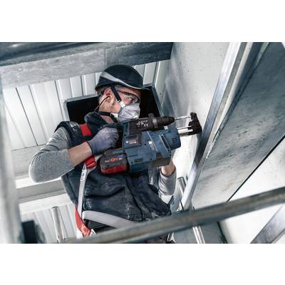 Ein Arbeiter mit Schutzkleidung und -ausrüstung benutzt eine Bohrmaschine, um in einer industriellen Umgebung an der Decke zu arbeiten.