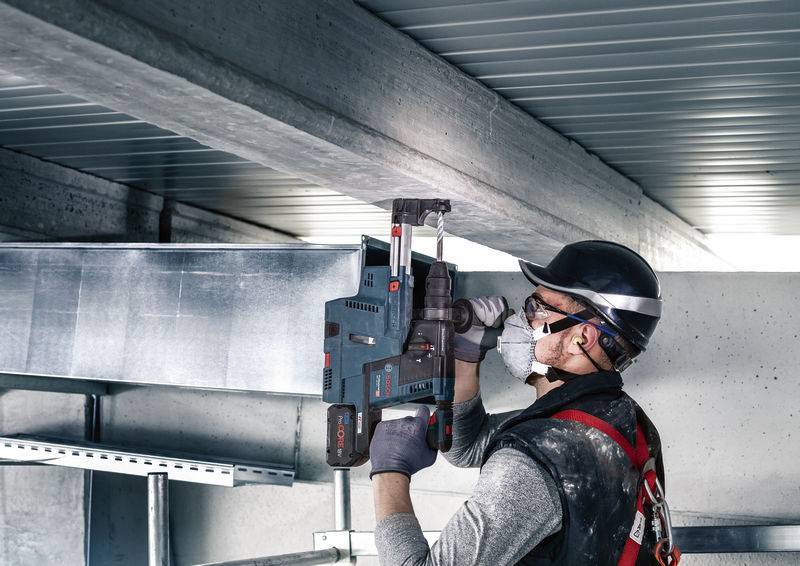 Ein Arbeiter in Schutzkleidung nutzt ein Elektrowerkzeug, um Metallstrukturen in einem industriellen Gebäude zu bearbeiten.