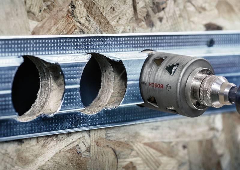 Bohrer schneidet Löcher in eine Metallschiene auf einer Holzplatte. Der Bohrer hat eine Aufschrift einer Werkzeugmarke.