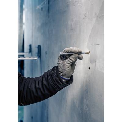 Person mit Handschuh schreibt mit einem Stift an eine graue Wand.