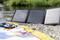 Ein tragbares Solarpanel liegt am Ufer eines Flusses auf Kieselsteinen. Daneben ein buntes Handtuch und ein geschlossenes Buch.