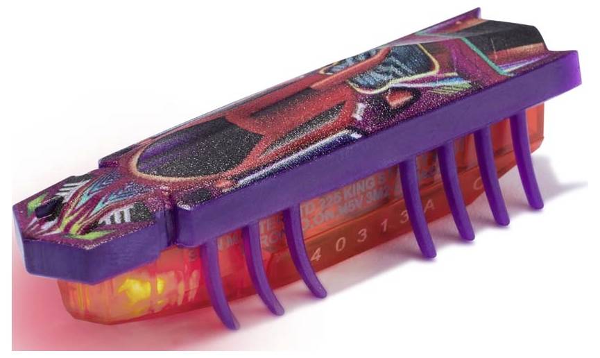 Ein kleiner, bunt bedruckter Spielzeugroboter in Insektenform mit lila Beinen und orangenem Gehäuse bewegt sich auf einer Oberfläche.