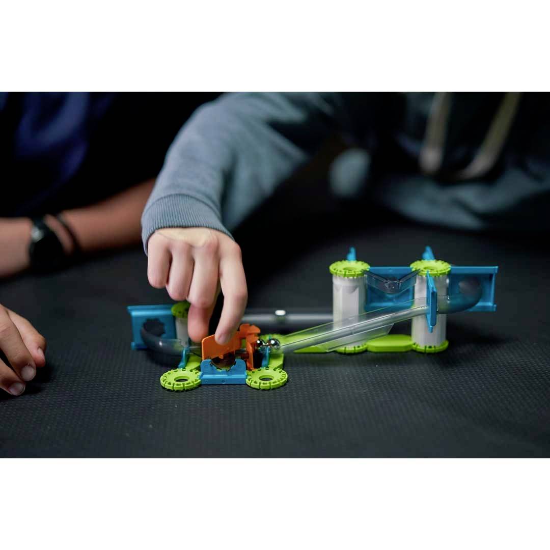 Zwei Personen bauen ein farbiges Modellfahrzeug aus Kunststoff auf einem Tisch zusammen, das mechanische Komponenten zeigt.