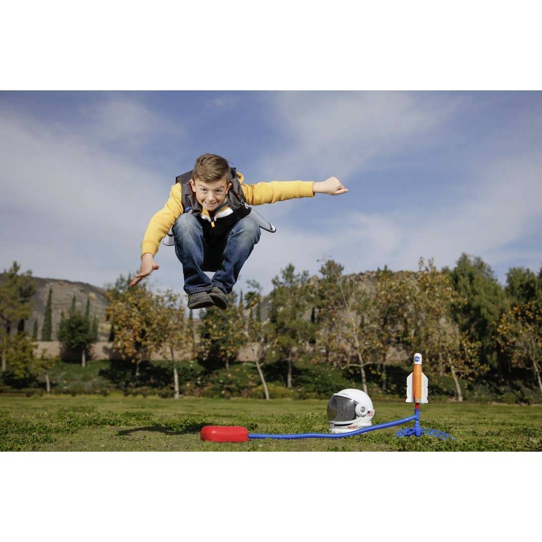 Ein Junge springt in einem Park, während eine Spielzeugrakete und ein Astronautenhelm auf dem Boden neben ihm liegen.