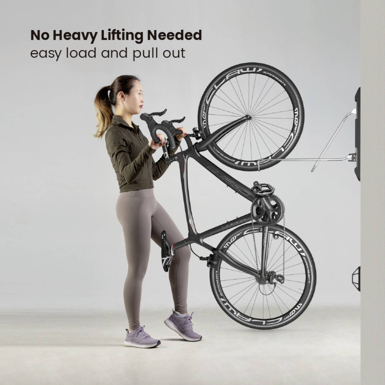 Eine Frau zieht ein Fahrrad an einer Wandhalterung heraus. Der Text lautet 'No Heavy Lifting Needed, easy load and pull out'.