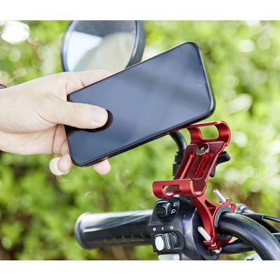 Person hält ein Smartphone über eine rote Fahrradhalterung, die an einem Fahrradlenker befestigt ist. Im Hintergrund sind grüne Blätter.