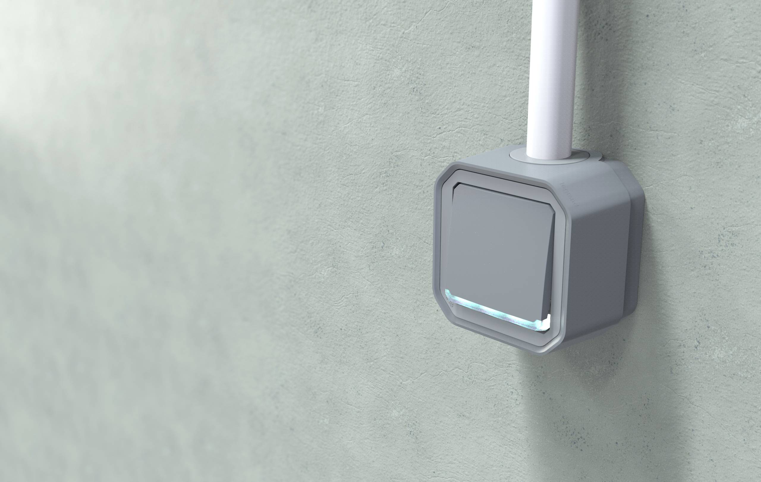 Ein grauer Sensor ist an einer Wand montiert. Ein Kabel führt nach oben. Er hat ein kleines leuchtendes Element an der Unterseite.