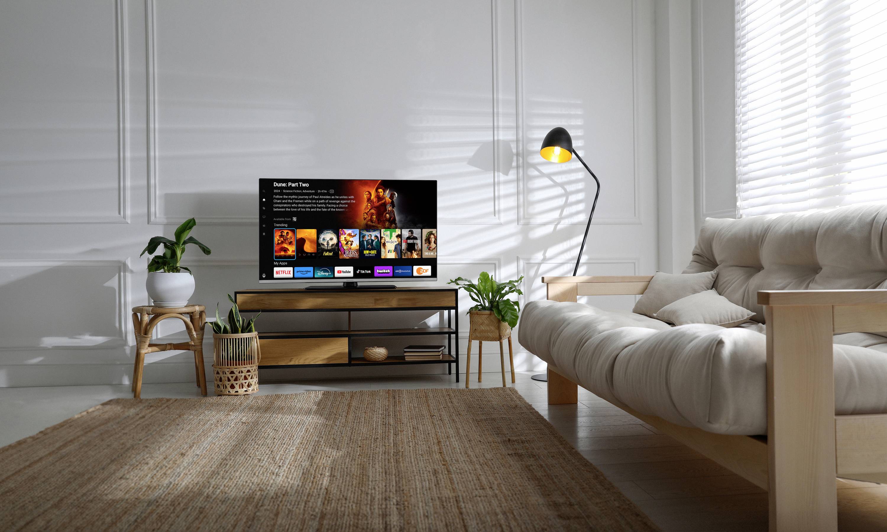 Ein Wohnzimmer mit einem Sofa, einem Teppich und einem Fernseher auf einem Tisch. Der Fernseher zeigt eine Streaming-App-Benutzeroberfläche.