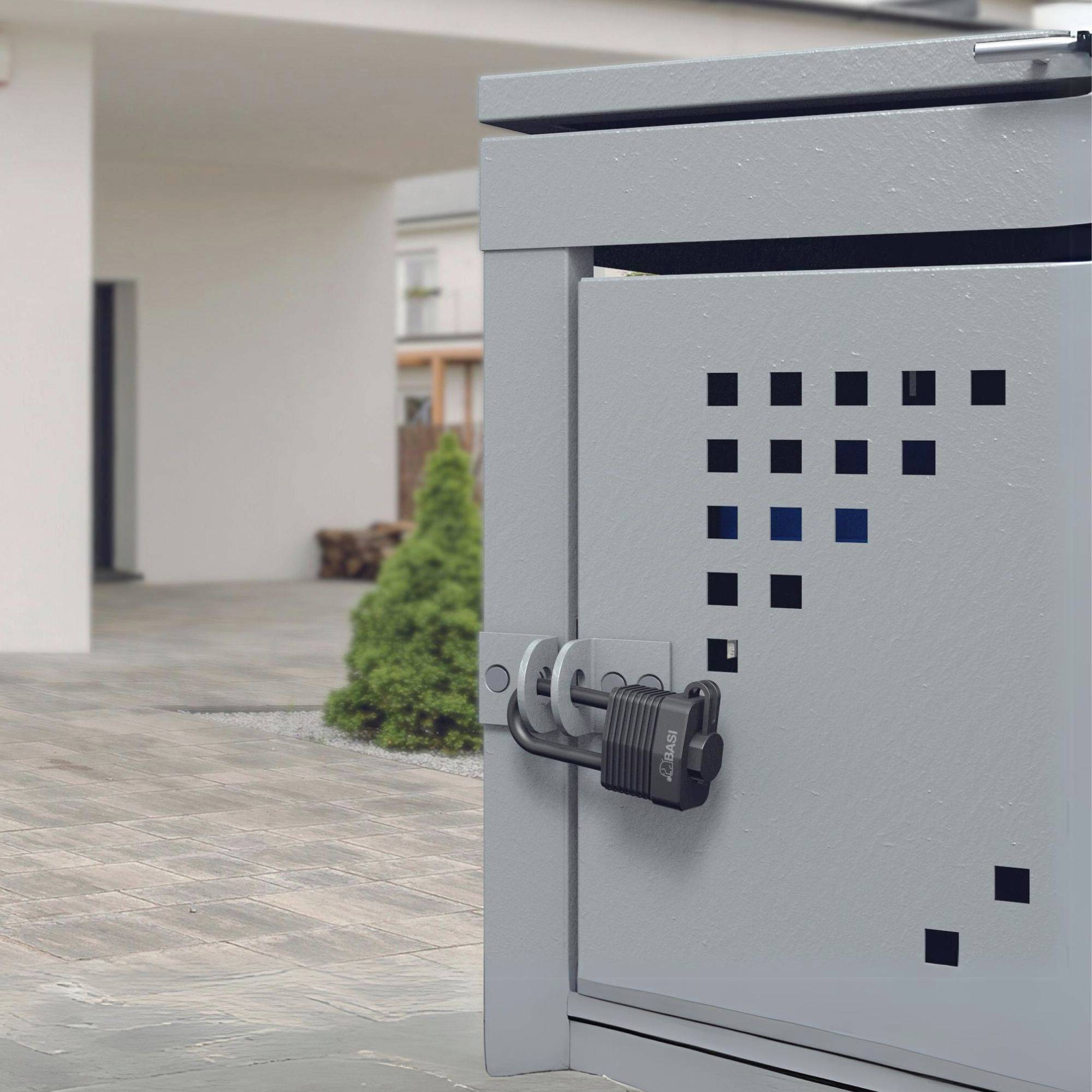 Ein sicherheitsgeschützter Briefkasten außerhalb eines Gebäudes, abgeschlossen mit einem Vorhängeschloss, auf einem gepflasterten Weg.