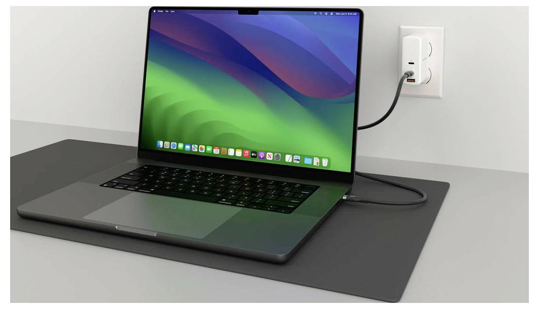 Ein Laptop mit buntem Bildschirm ist über ein Kabel an eine Steckdose angeschlossen und steht auf einem grauen Tisch.