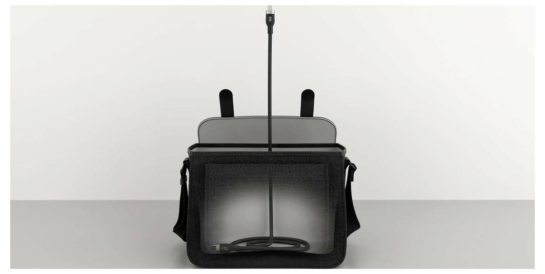 Eine schwarze Umhängetasche mit offenem Deckel steht auf einem Tisch. Ein Kabel ragt aus der Tasche nach oben.