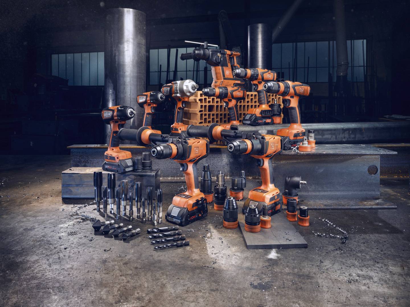 Ein Sortiment von orangefarbenen Elektrowerkzeugen und Zubehör, wie Bohrer und Aufsätze, auf einer Werkbank in einer Werkstatt.