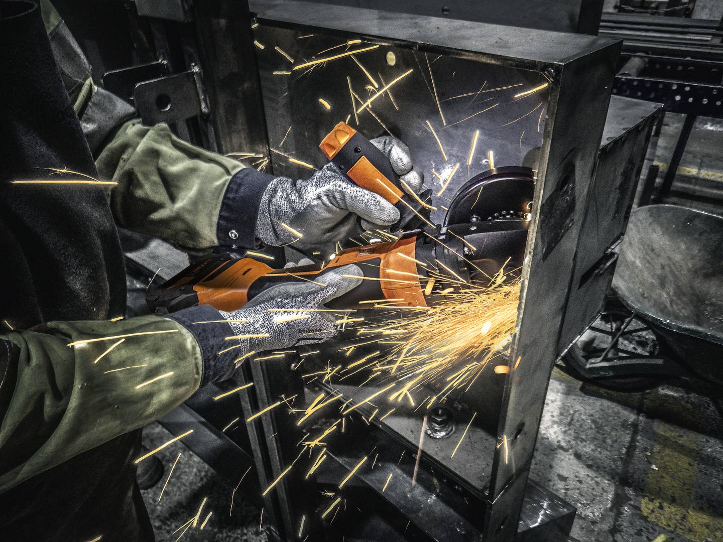 Ein Arbeiter schleift Metall mit einem Winkelschleifer. Funken fliegen in einem Werkstattumfeld. Schutzkleidung ist sichtbar.