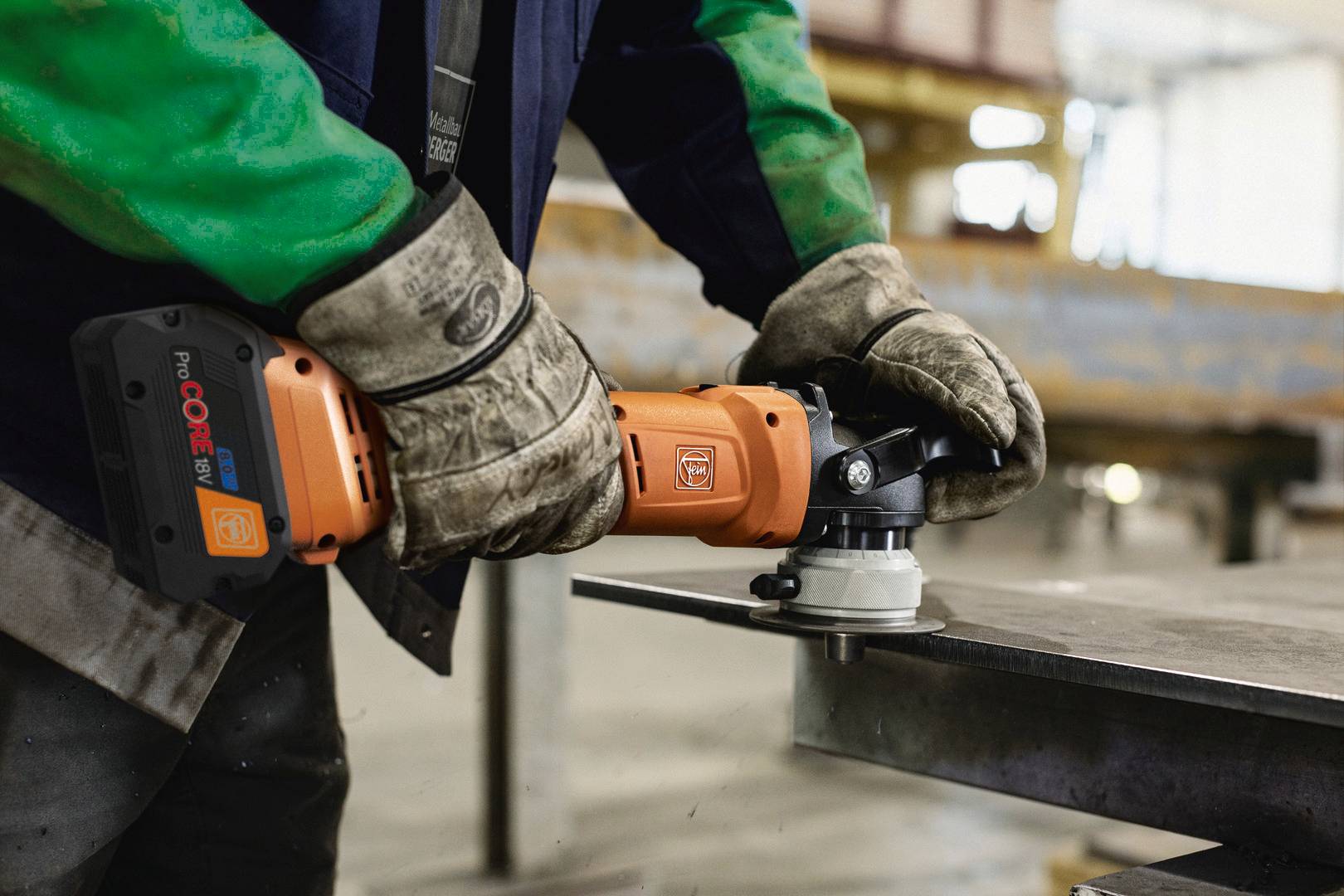 'Arbeiter schleift Metallplatte mit einer orangefarbenen Schleifmaschine in einer Werkstatt.'