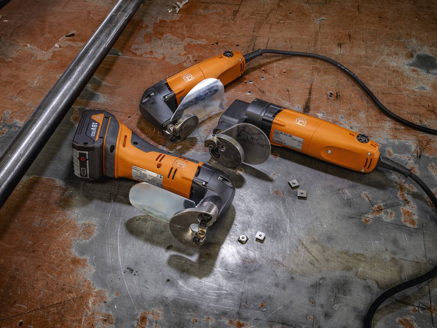 Drei orangefarbene Elektrowerkzeuge auf einer Werkbank. Sie sind mit Metallblättern ausgestattet und miteinander verkabelt.