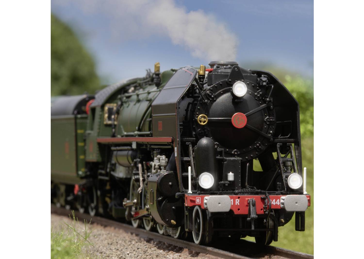 Eine alte Dampflokomotive auf einem Bahngleis, umgeben von grünem Bewuchs, unter klarem Himmel. Die Lokomotive ist dunkelgrün und schwarz.