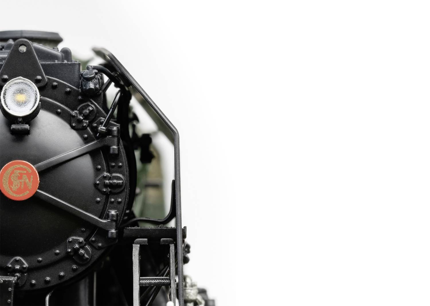 Nahaufnahme einer schwarzen Dampflokomotive gegen einen weißen Hintergrund. Das Bild zeigt die Frontansicht mit einer runden Tür und einem Licht.