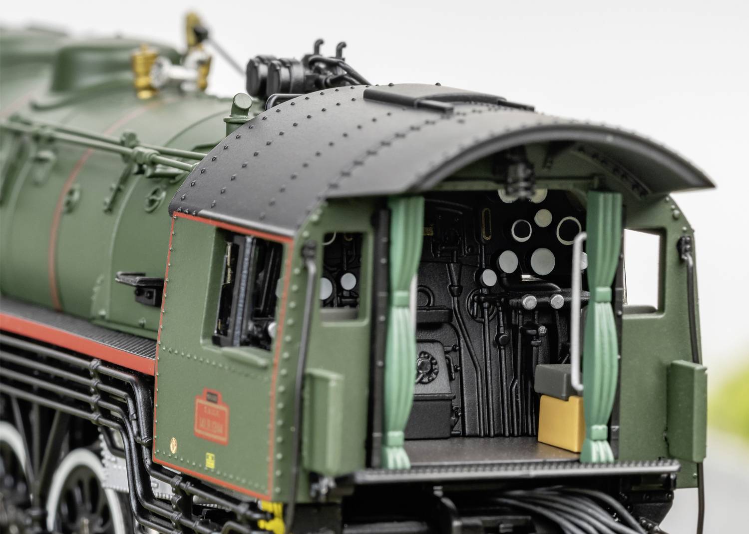 Nahaufnahme der Führerstand einer alten Dampflokomotive mit grünen Vorhängen und detaillierten Armaturen im Inneren.