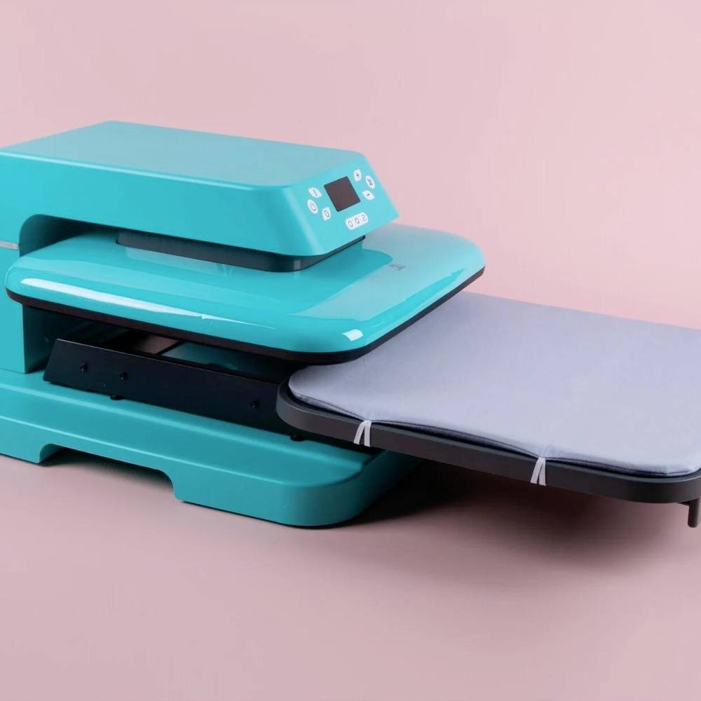 Ein türkisfarbener Drucker oder Plotter auf einem rosa Hintergrund. Der Drucker hat ein digitales Display und eine erweiterte Druckfläche.