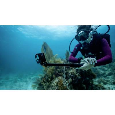 Eine Taucherin unter Wasser filmt ein Korallenriff mit einer Action-Kamera an einem Selfie-Stick. Sie trägt eine Taucherbrille und Atemgerät.