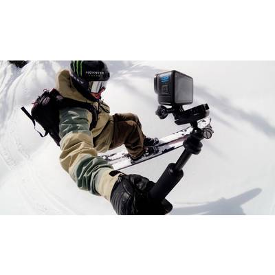 Ein Snowboarder fährt durch frischen Pulverschnee, hält eine Action-Kamera auf einem Selfie-Stick, um die Fahrt zu filmen.