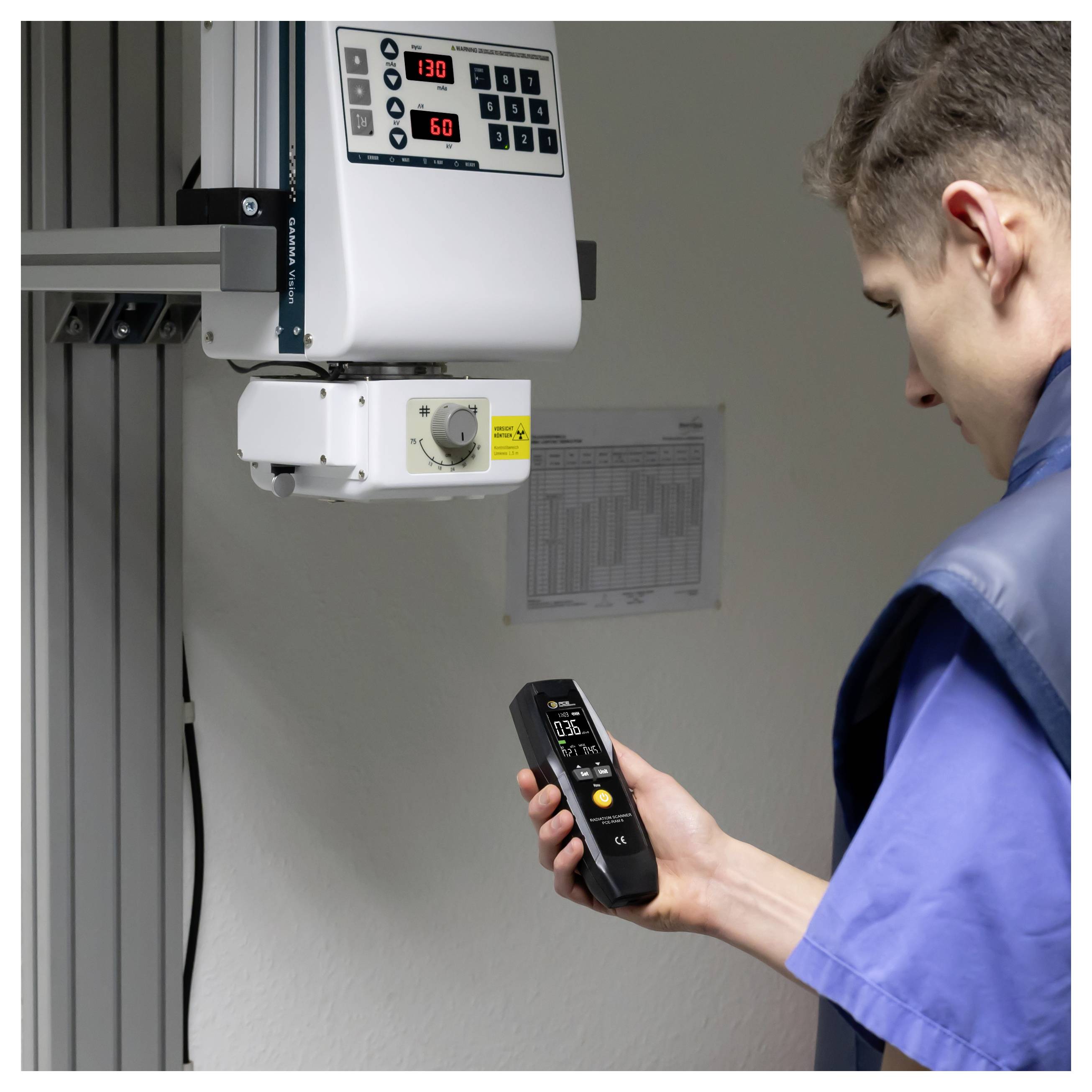Techniker, der mit einem tragbaren Messgerät ein an der Wand montiertes Industriegerät mit digitaler Anzeige und Bedienungselementen überprüft.